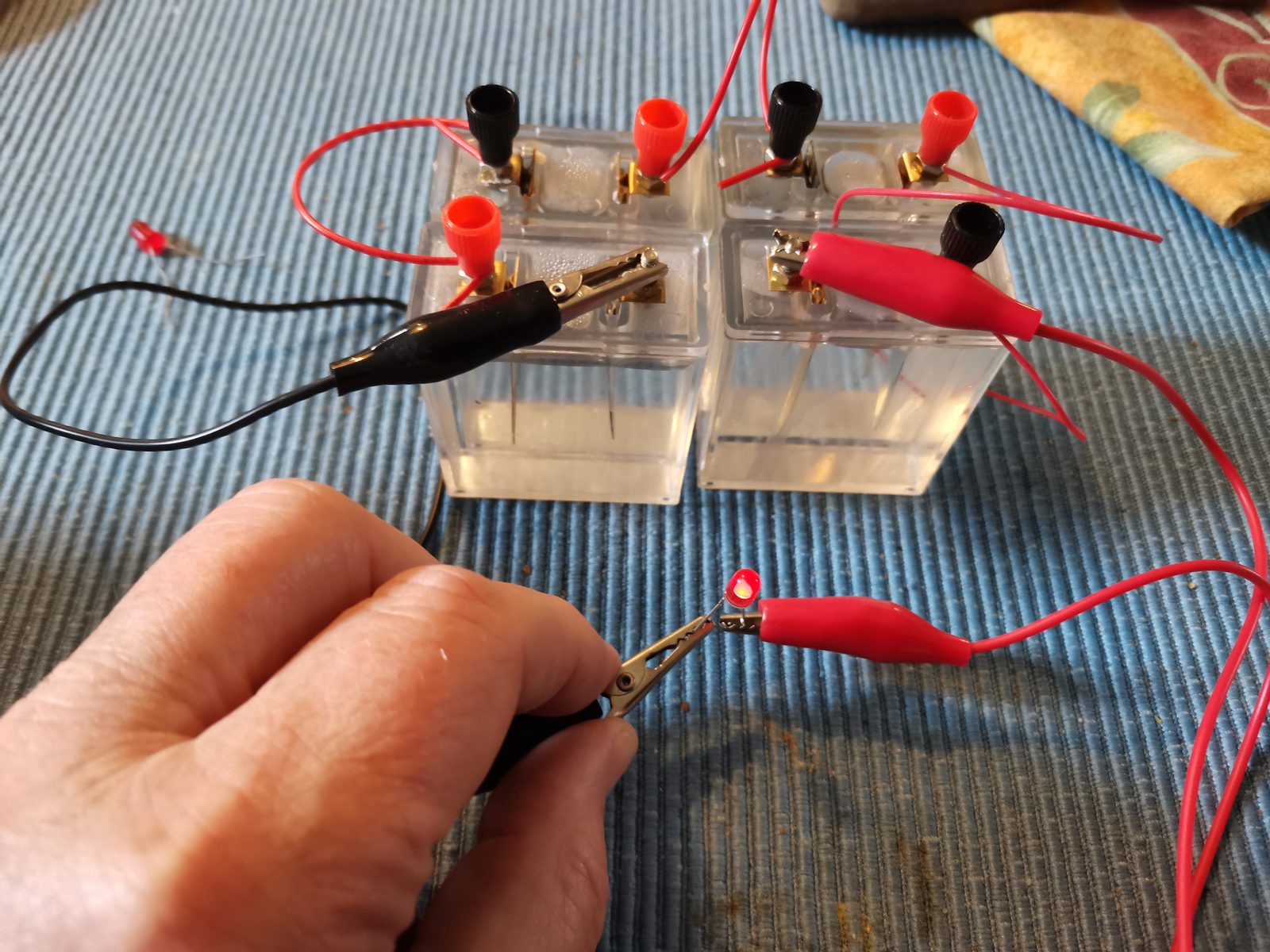 Fire gennemsigtige celler med elektroder i saltvand, forbundet i serie med røde og sorte ledninger, og en rød lysdiode der lyser